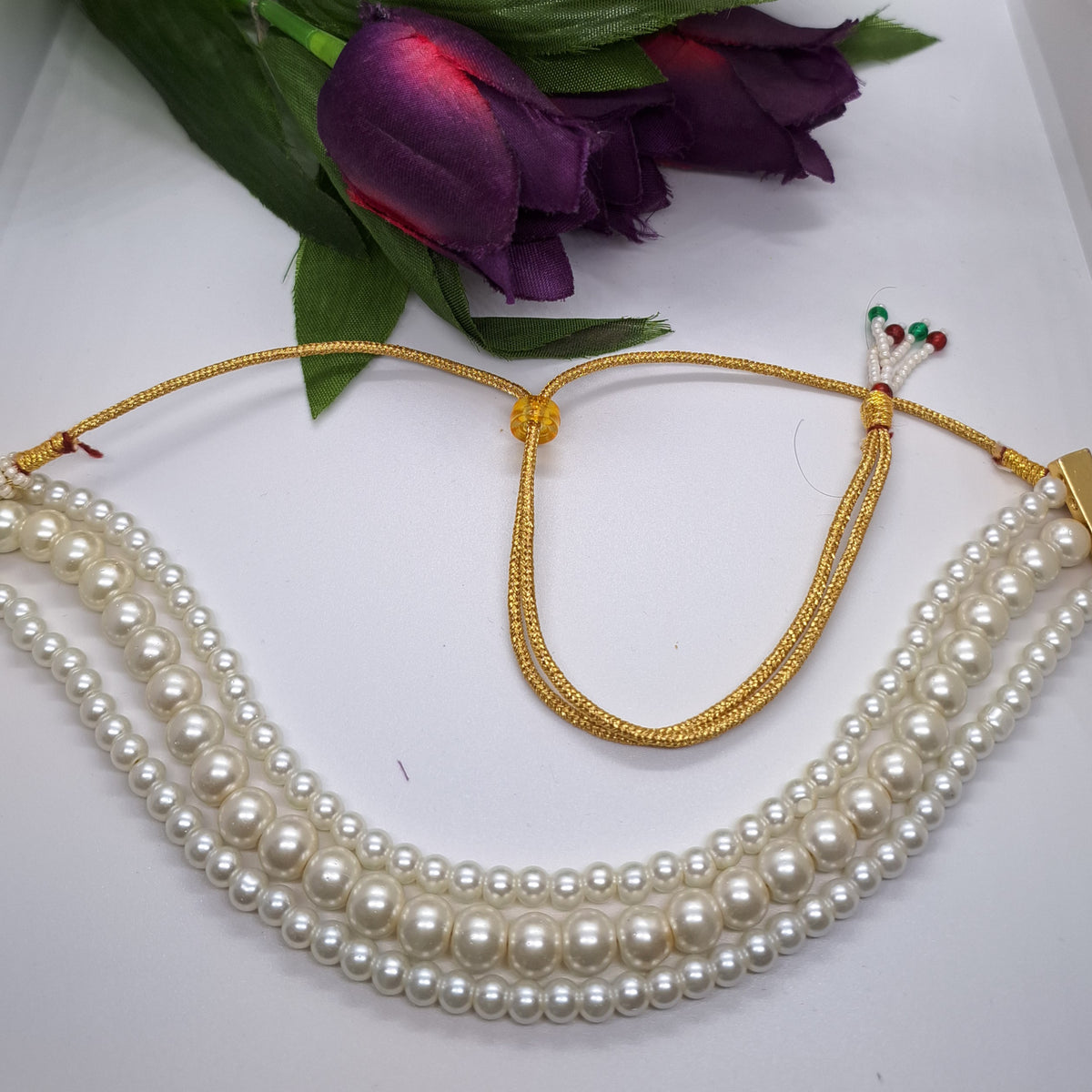 Three strand pearl choker necklace with gold adjustable clasp, displayed with purple flowers