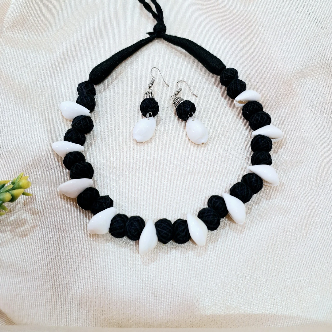 Handmade black thread necklace and earrings set with white beads on cream fabric