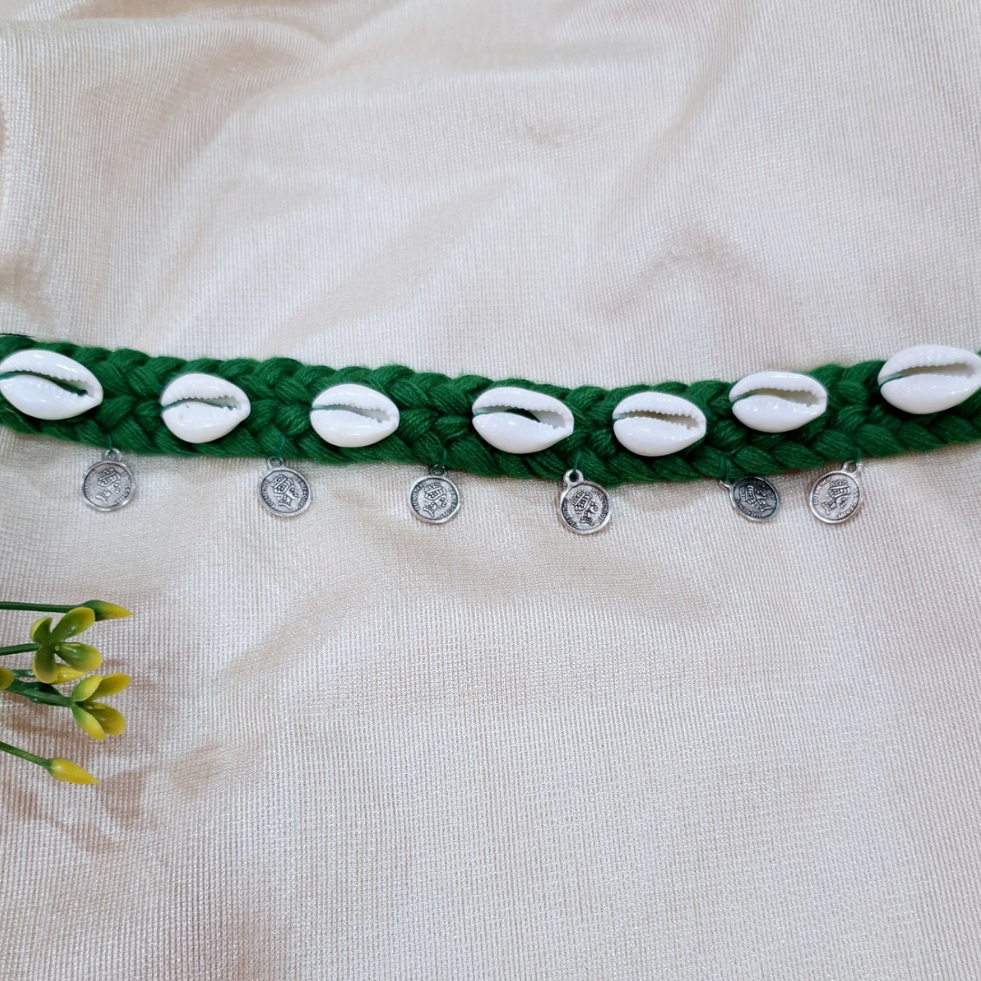 Handmade green braided waist belt with cowrie shells and small silver coins on fabric