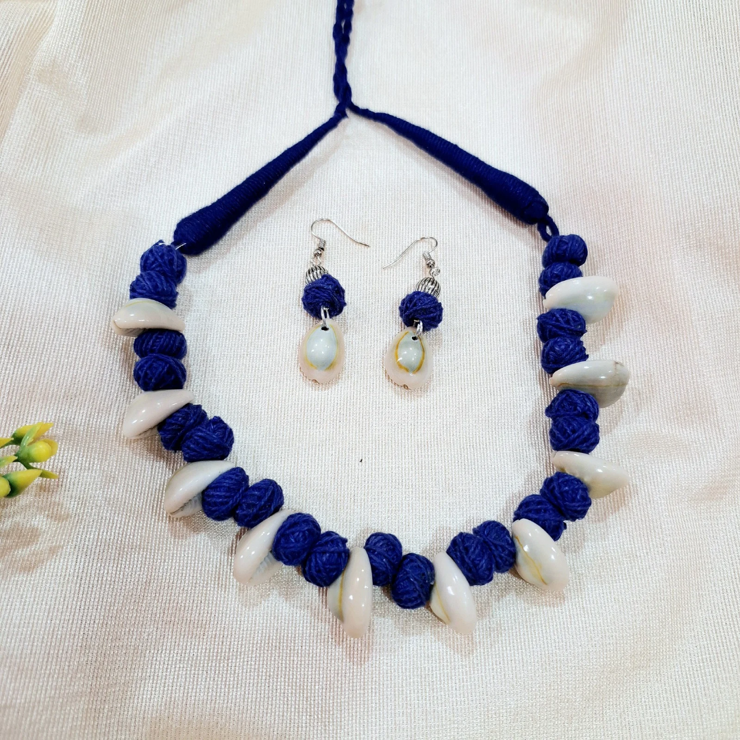 Handmade blue thread and shell necklace with matching shell drop earrings on cream fabric