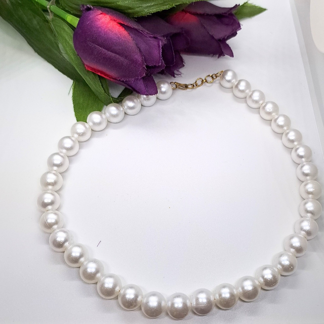 White pearl necklace with gold clasp displayed beside artificial purple roses on white background