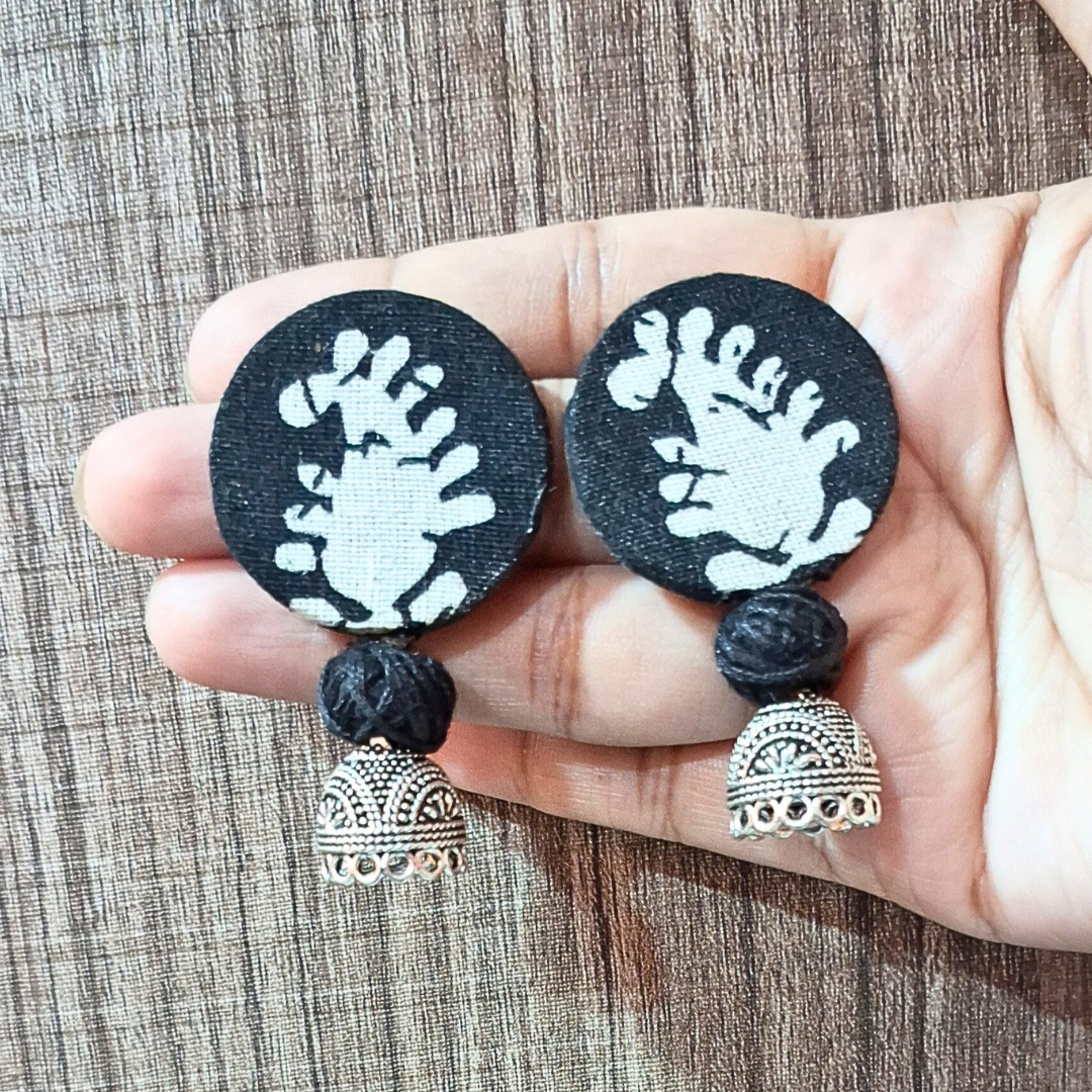 Hand holding black and white round fabric jhumka earrings with silver bell charms