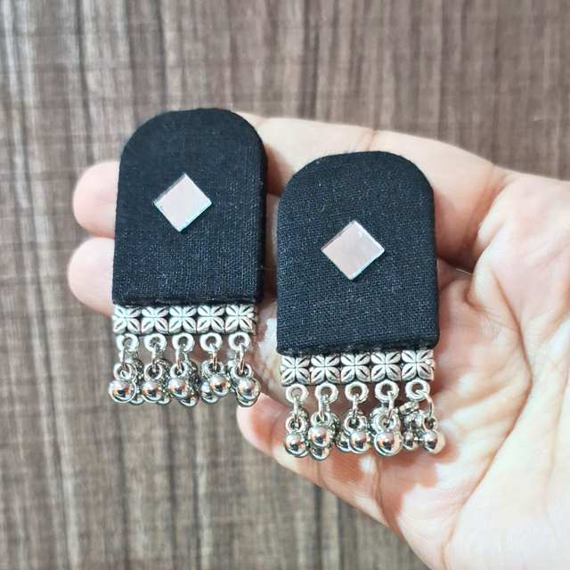 Hand holding black fabric earrings with silver square accent and dangling beads
