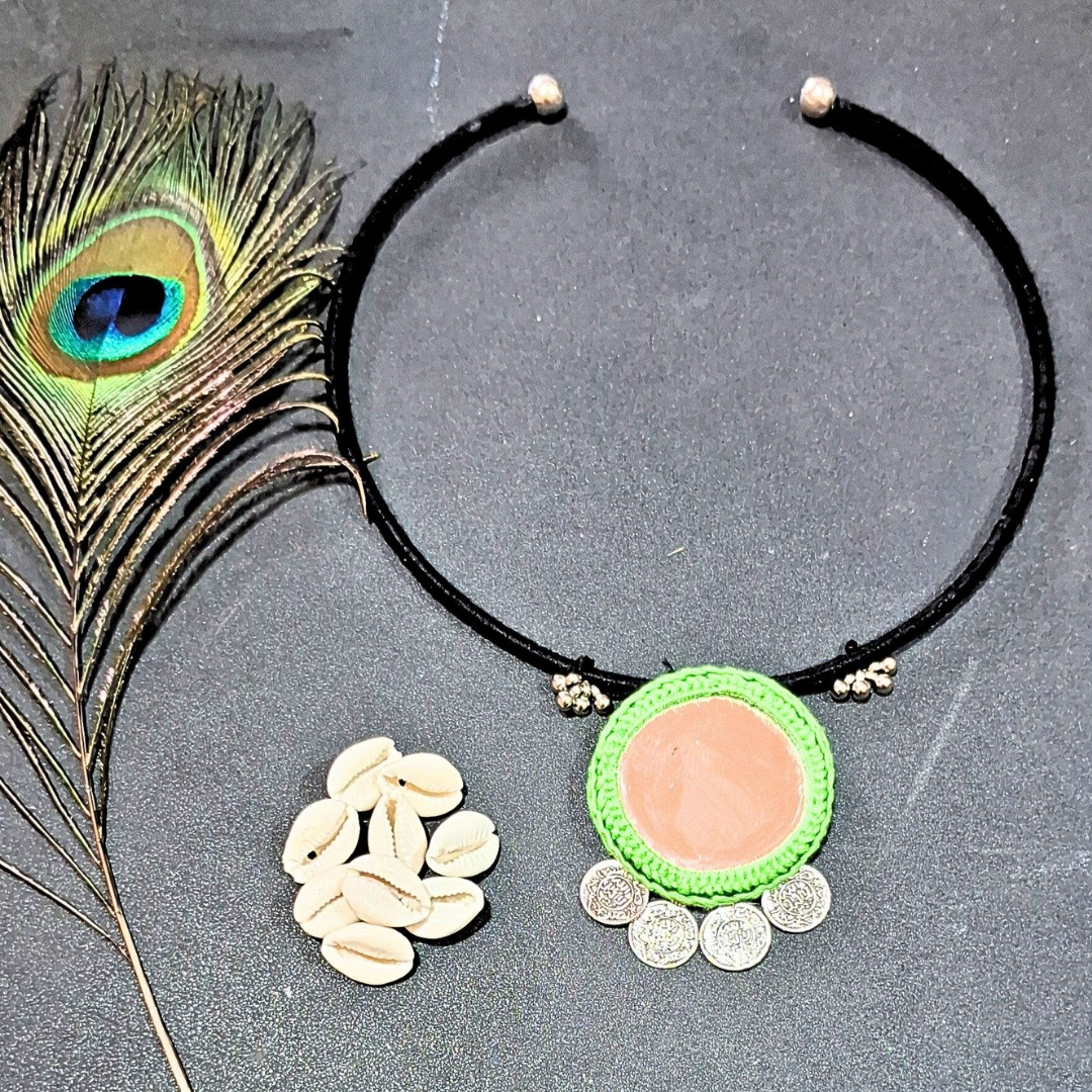 Handmade pendant necklace with green border, silver coins, next to cowrie shells and peacock feather