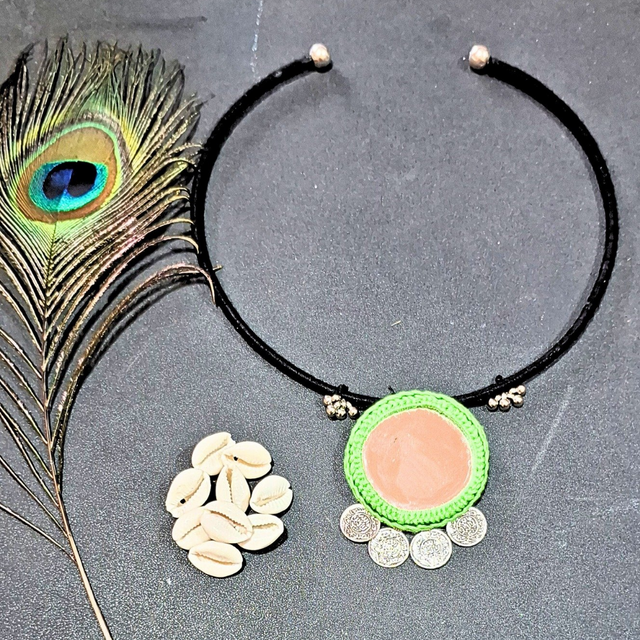 Handmade pendant necklace with green border, silver coins, next to cowrie shells and peacock feather