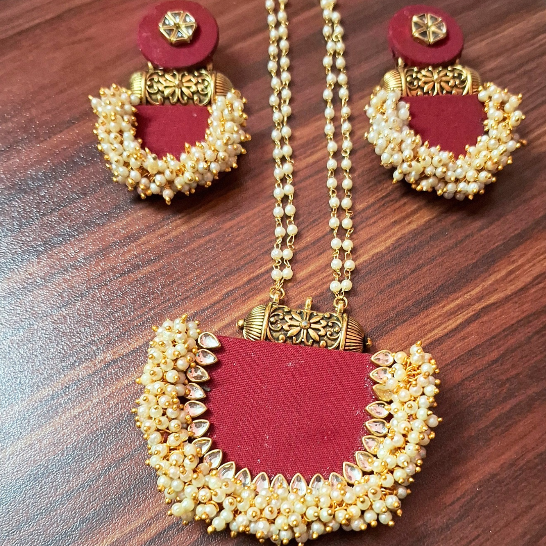 Traditional red and gold necklace set with pearl beads and matching earrings on wooden surface