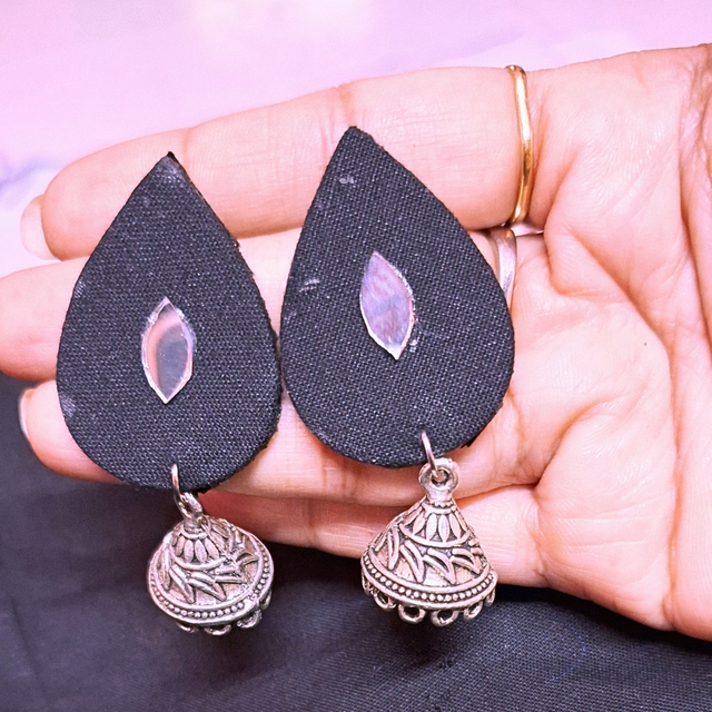 Hand holding black fabric teardrop earrings with silver jhumka and shell inlay