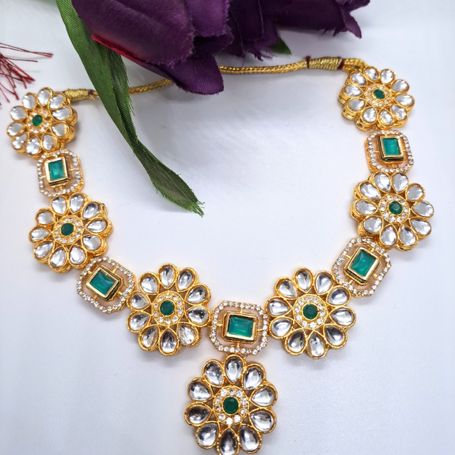 Gold plated floral necklace with green gemstone accents and white crystals on white background