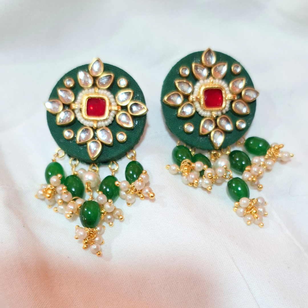 Green and gold ethnic earrings with red center stone, pearl and bead danglers on white fabric