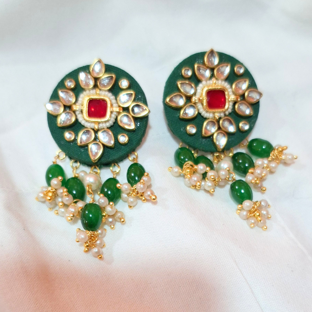 Green and gold ethnic earrings with red center stone, pearl and bead danglers on white fabric
