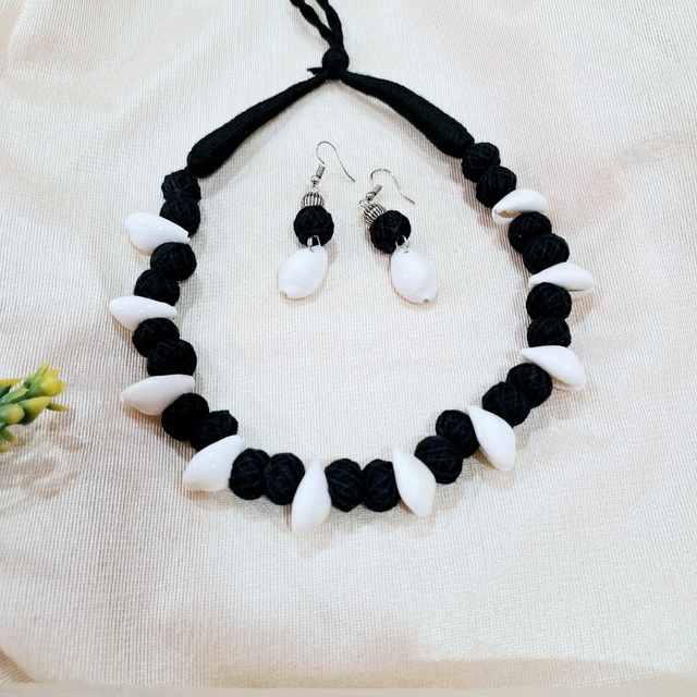 Handmade black thread necklace and earrings set with white beads on cream fabric