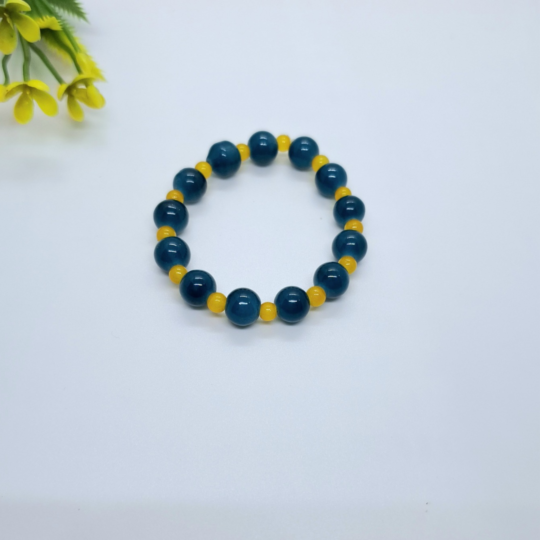 Blue and yellow beaded bracelet on white background with small plant decor