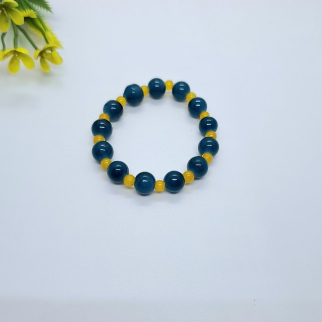 Blue and yellow beaded bracelet on white background with small plant decor