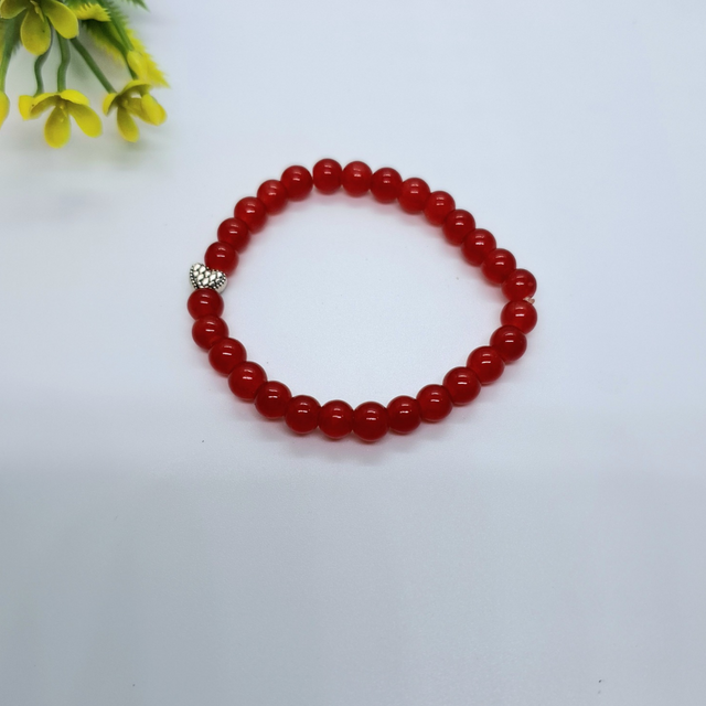 Red beaded bracelet with silver heart charm on white background, closeup jewelry photo