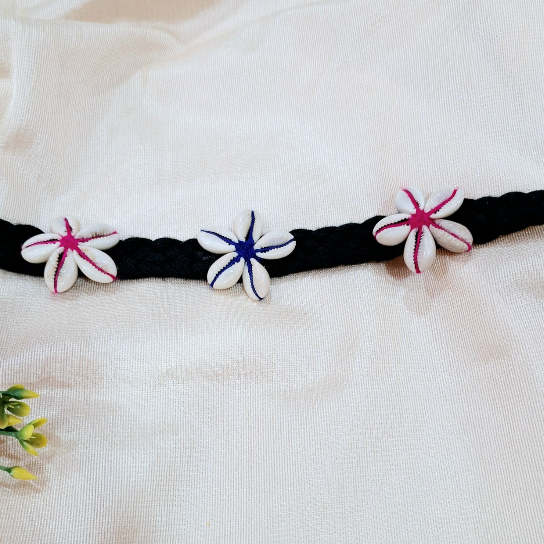 Handmade black braided belt with cowrie shell flower accents on white fabric background