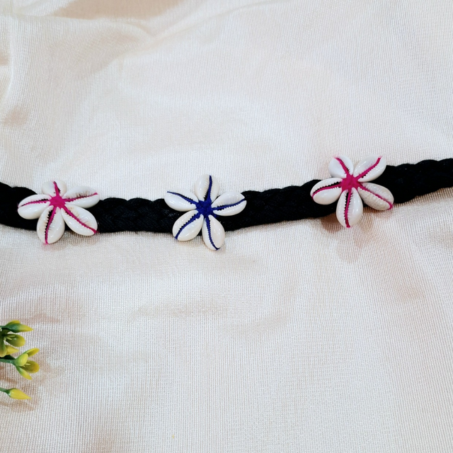 Handmade black braided belt with cowrie shell flower accents on white fabric background