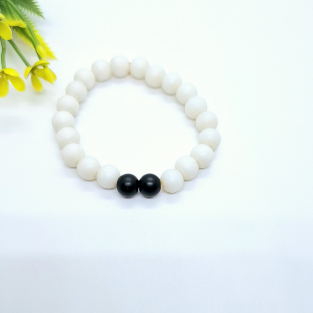 Minimalist white beaded bracelet with two black accent beads on white background
