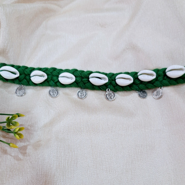 Handmade green braided waist belt with cowrie shells and small silver coins on fabric
