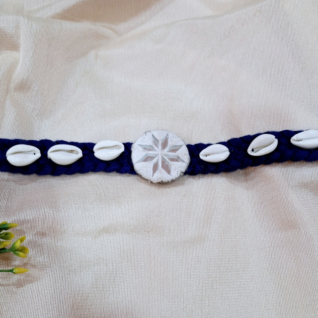 Handmade blue braided bracelet with cowrie shells and a central white embroidered motif