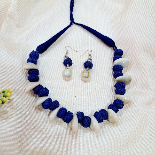 Handmade blue thread and shell necklace with matching shell drop earrings on cream fabric