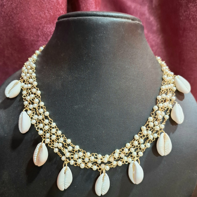 Handmade gold chain necklace with cowrie shells and small pearls on black display bust